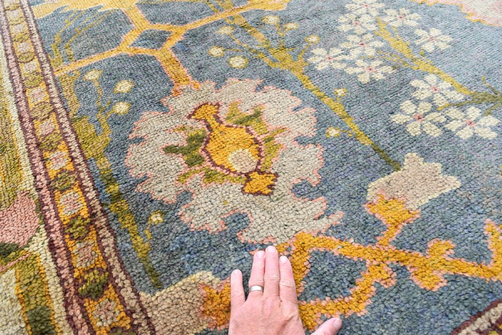 A large hand-knotted Gavin Morton Donegal wool carpet featuring stylised floral motifs in pink, ochre, and green across a slate blue field. View X