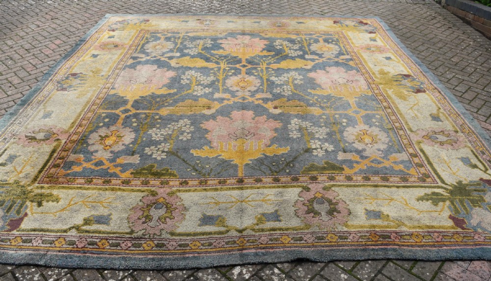 A large hand-knotted Gavin Morton Donegal wool carpet featuring stylised floral motifs in pink, ochre, and green across a slate blue field. View XI