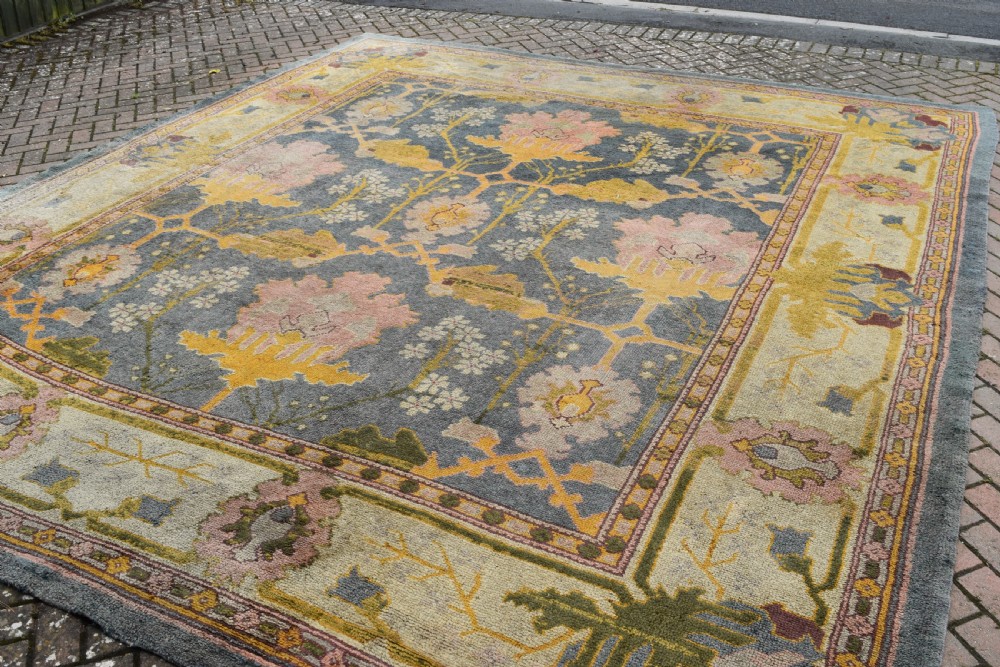 A large hand-knotted Gavin Morton Donegal wool carpet featuring stylised floral motifs in pink, ochre, and green across a slate blue field. View XII
