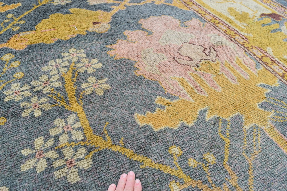 A large hand-knotted Gavin Morton Donegal wool carpet featuring stylised floral motifs in pink, ochre, and green across a slate blue field. View XIII