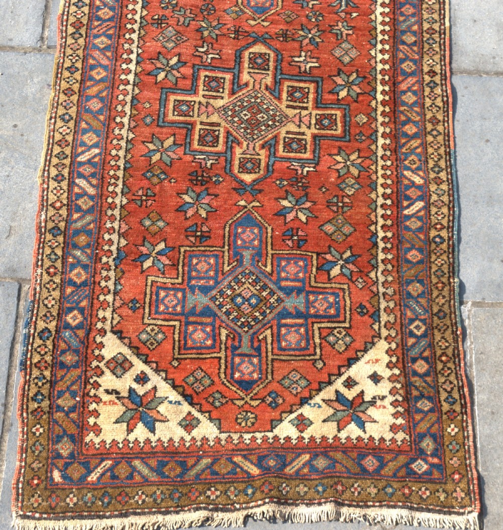 An antique Persian Heriz wool runner rug featuring repeating geometric medallions on a terracotta red field with blue and cream borders. View II