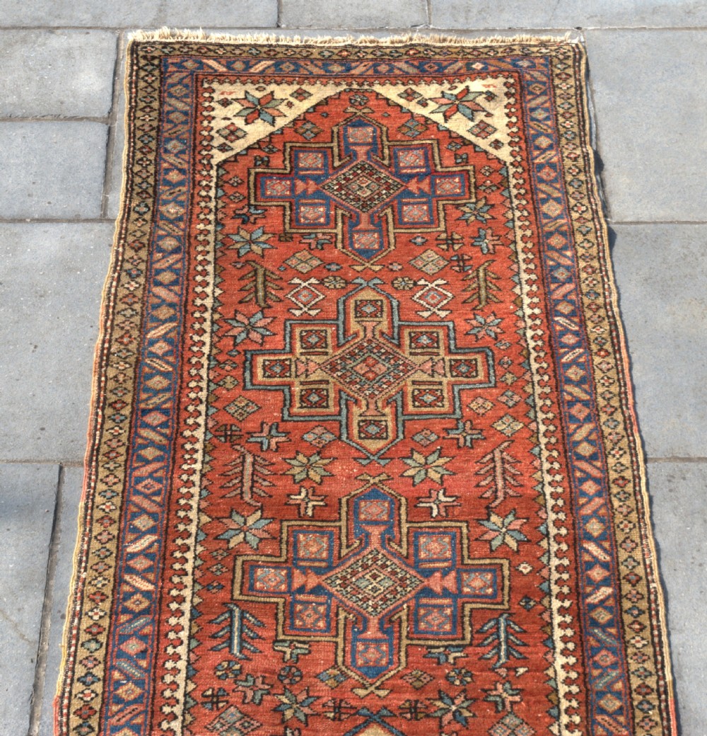 An antique Persian Heriz wool runner rug featuring repeating geometric medallions on a terracotta red field with blue and cream borders. View IV