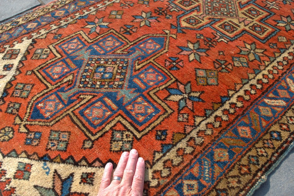 An antique Persian Heriz wool runner rug featuring repeating geometric medallions on a terracotta red field with blue and cream borders. View VI