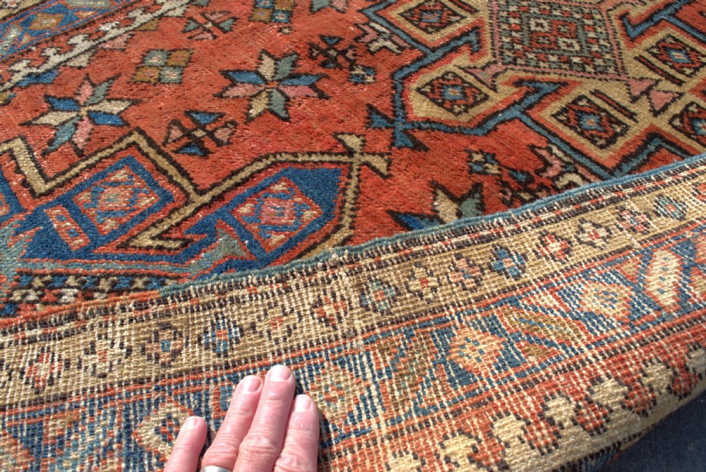 An antique Persian Heriz wool runner rug featuring repeating geometric medallions on a terracotta red field with blue and cream borders. View VII