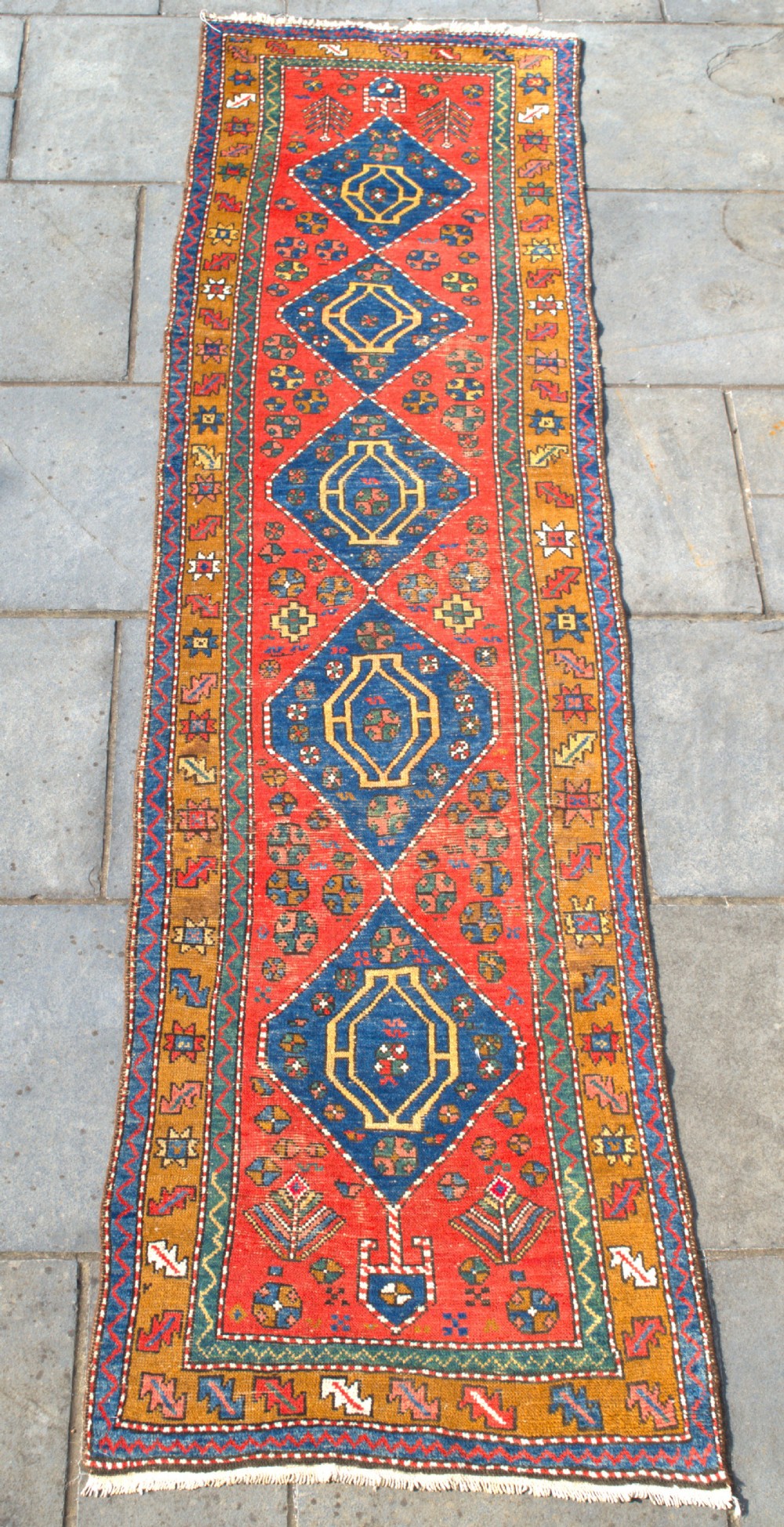 An antique hand-knotted Persian Heriz runner rug featuring five blue diamond medallions along a red field with ochre borders.