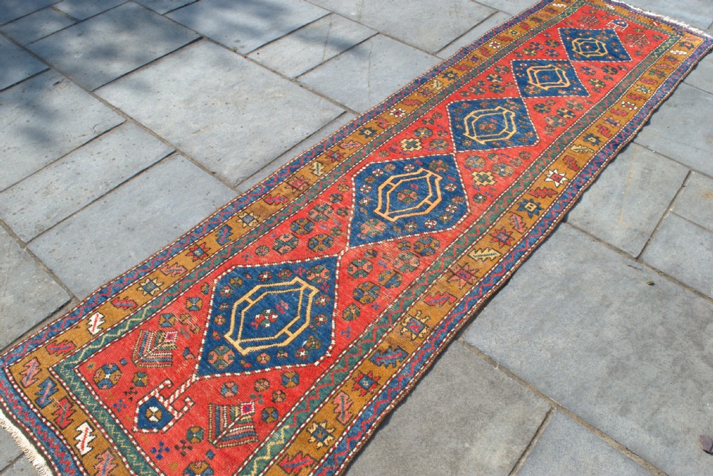An antique hand-knotted Persian Heriz runner rug featuring five blue diamond medallions along a red field with ochre borders. View III