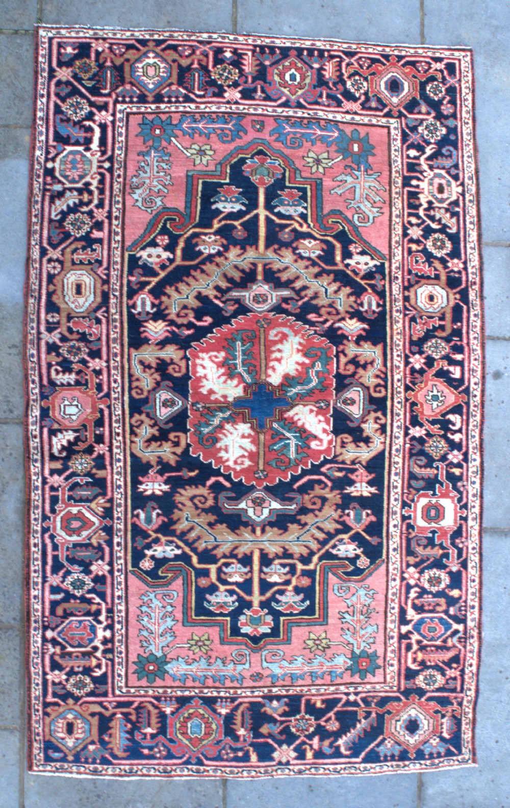 An antique hand-knotted Persian Heriz wool rug featuring a geometric central medallion in terracotta and blue on a navy field framed by a detailed border.