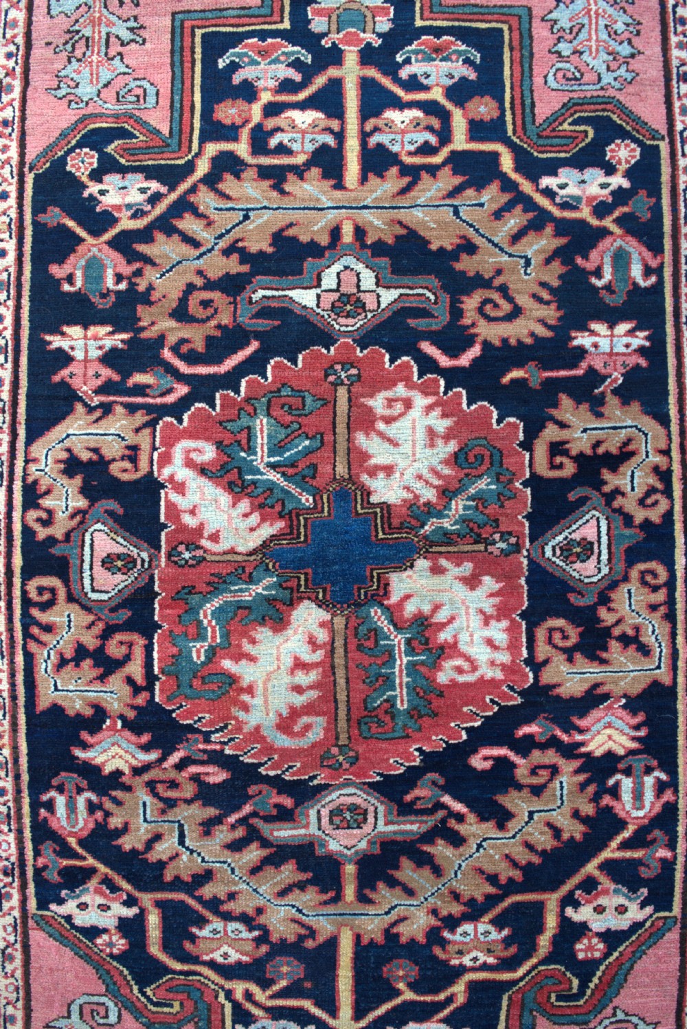 An antique hand-knotted Persian Heriz wool rug featuring a geometric central medallion in terracotta and blue on a navy field framed by a detailed border. View III