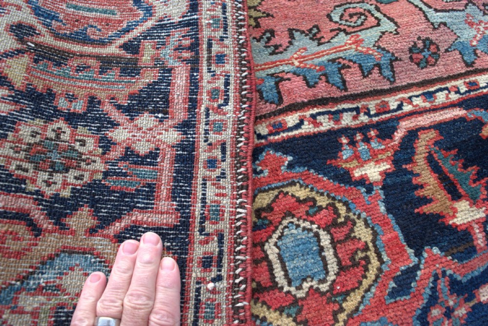 An antique hand-knotted Persian Heriz wool rug featuring a geometric central medallion in terracotta and blue on a navy field framed by a detailed border. View V