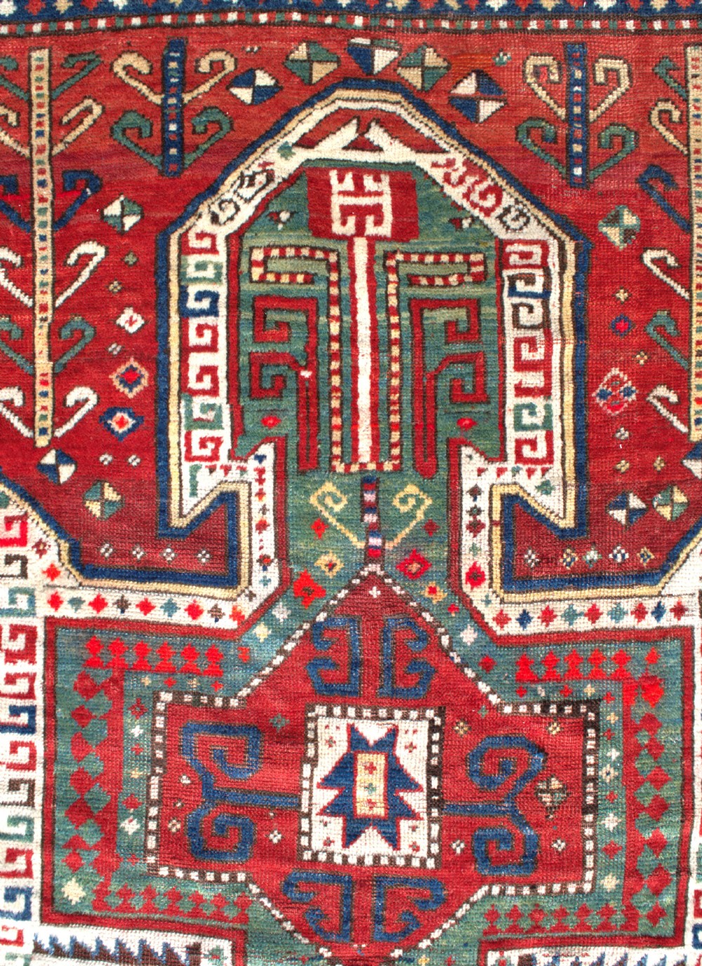 An antique hand-knotted Caucasian Sewan Kazak wool rug featuring a green central shield motif on a red ground with geometric borders. View II