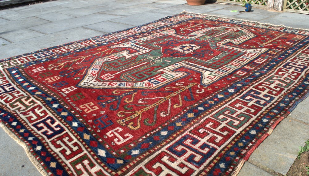 An antique hand-knotted Caucasian Sewan Kazak wool rug featuring a green central shield motif on a red ground with geometric borders. View III
