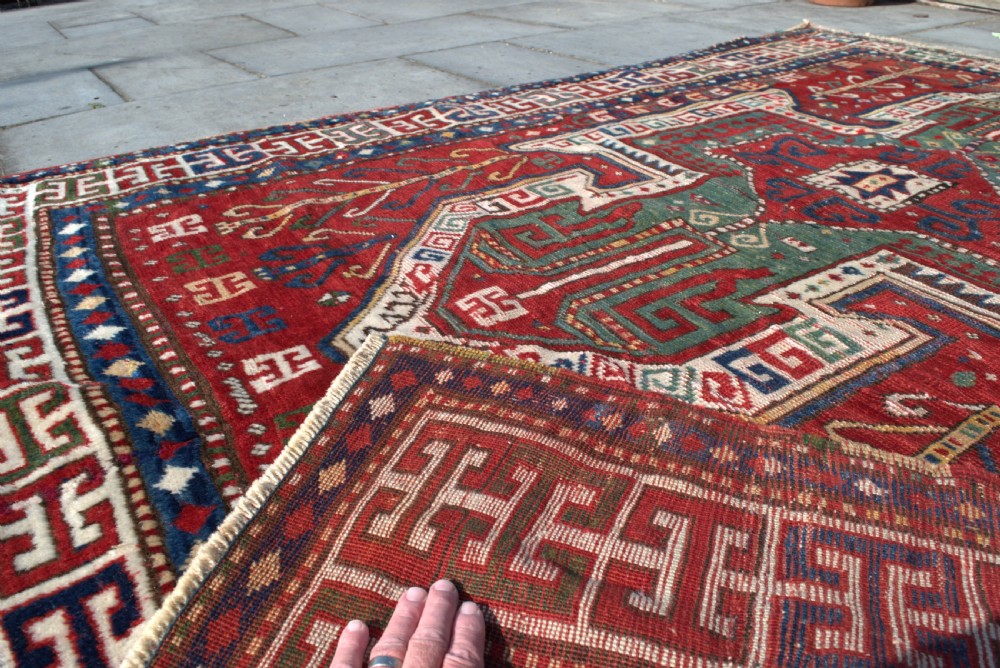 An antique hand-knotted Caucasian Sewan Kazak wool rug featuring a green central shield motif on a red ground with geometric borders. View IV