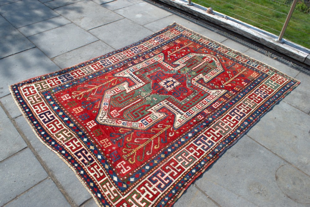An antique hand-knotted Caucasian Sewan Kazak wool rug featuring a green central shield motif on a red ground with geometric borders. View V