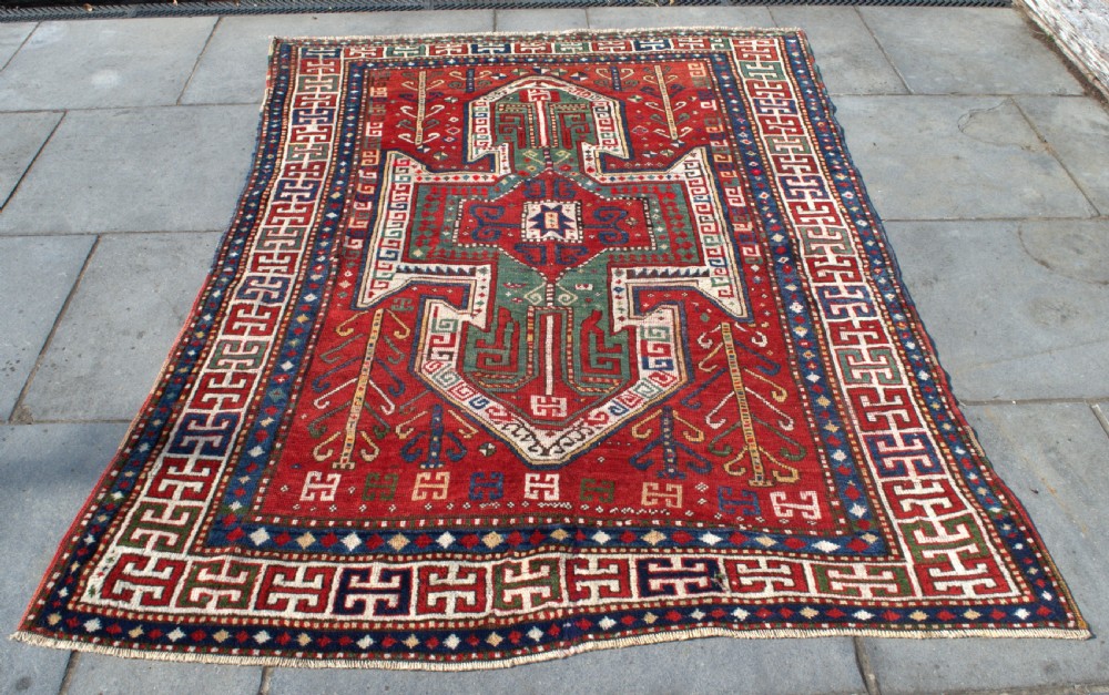 An antique hand-knotted Caucasian Sewan Kazak wool rug featuring a green central shield motif on a red ground with geometric borders. View VI