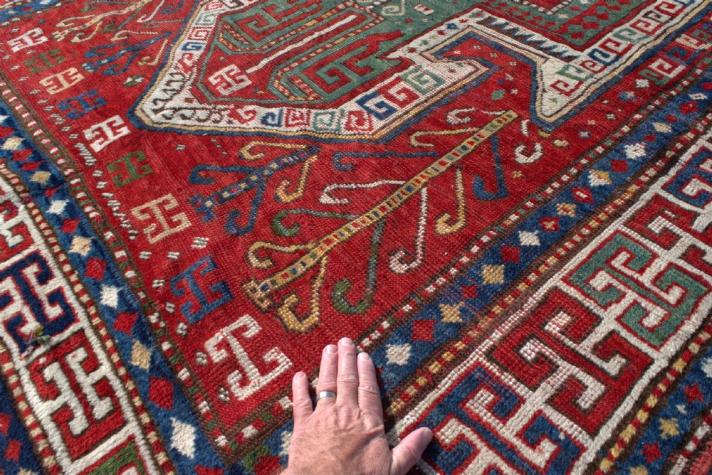 An antique hand-knotted Caucasian Sewan Kazak wool rug featuring a green central shield motif on a red ground with geometric borders. View VII