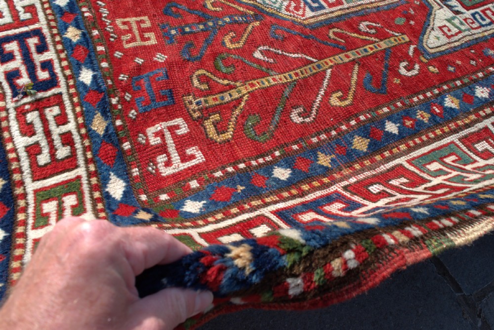 An antique hand-knotted Caucasian Sewan Kazak wool rug featuring a green central shield motif on a red ground with geometric borders. View VIII