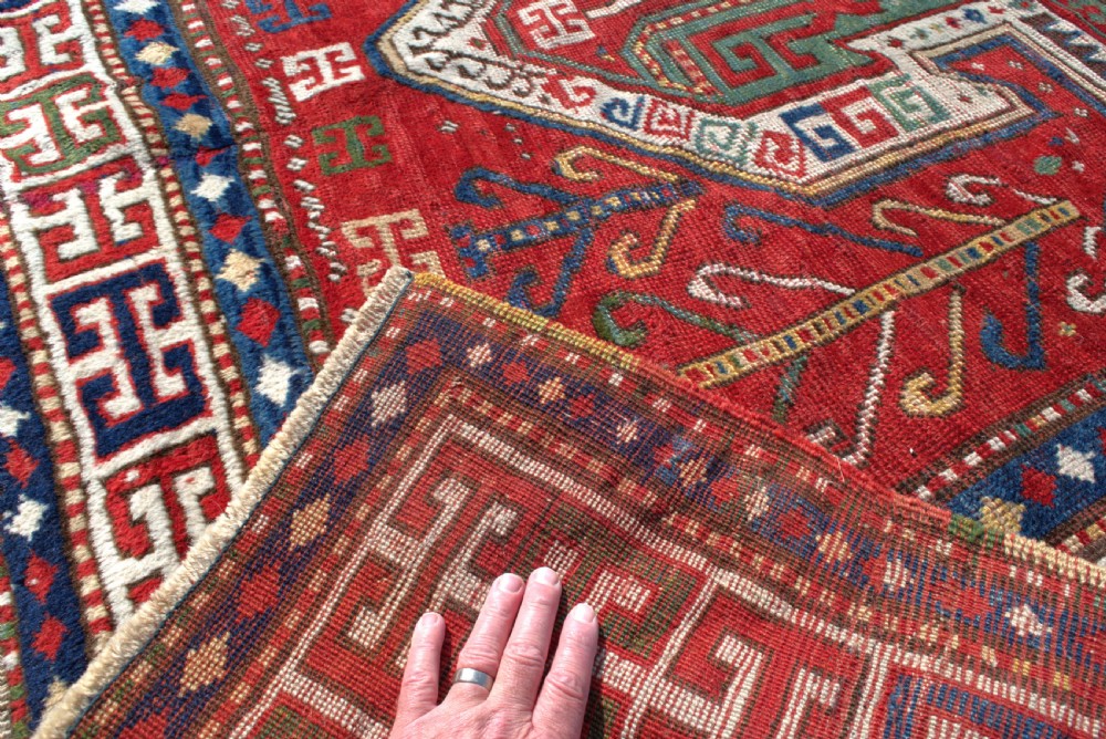 An antique hand-knotted Caucasian Sewan Kazak wool rug featuring a green central shield motif on a red ground with geometric borders. View IX