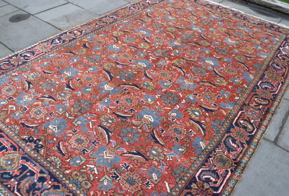 An antique hand-knotted Persian Heriz wool carpet featuring a dense geometric floral pattern on a rust red field with a dark blue ornamental border. View III