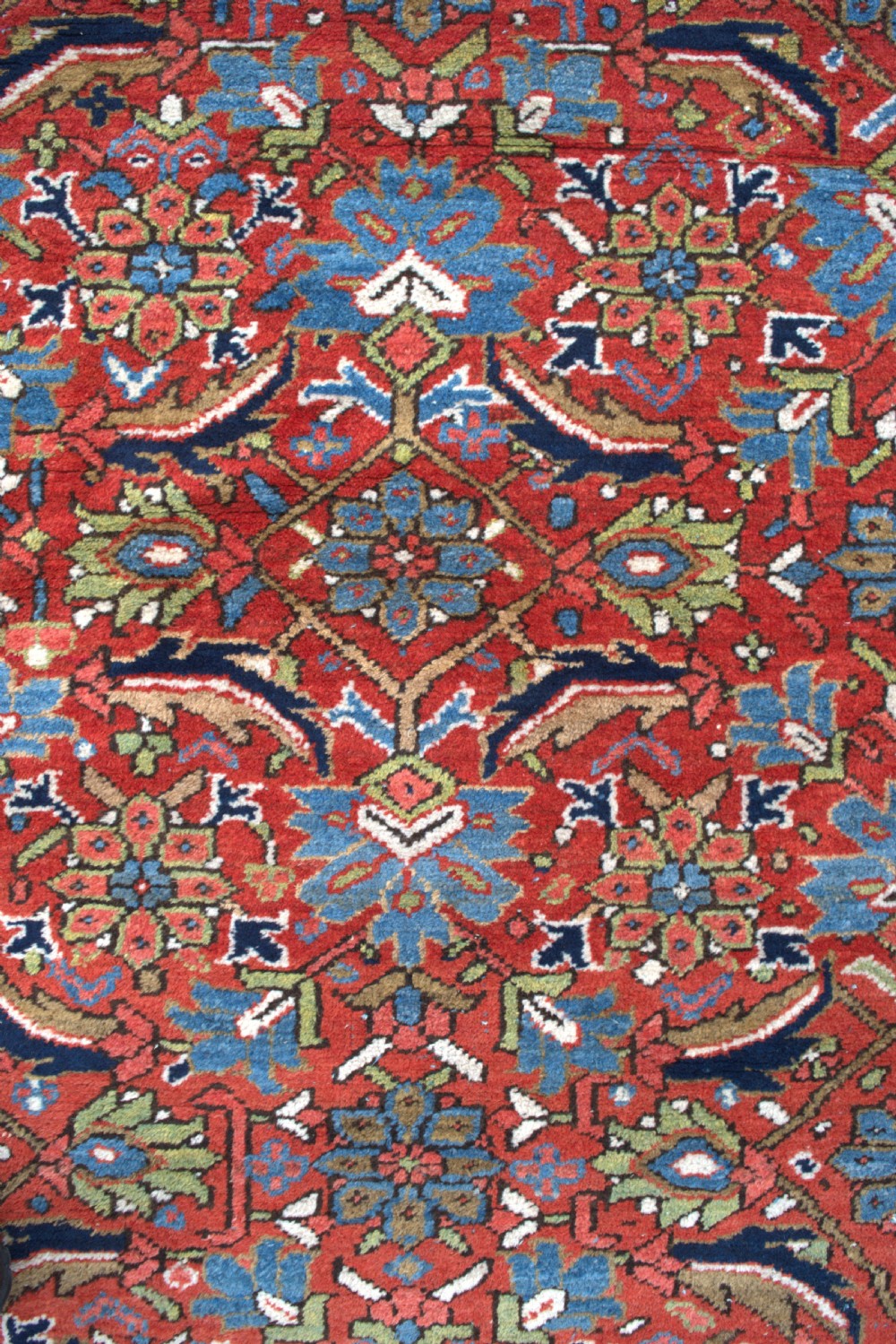 An antique hand-knotted Persian Heriz wool carpet featuring a dense geometric floral pattern on a rust red field with a dark blue ornamental border. View IV