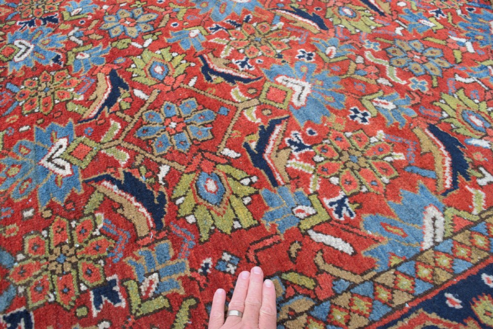 An antique hand-knotted Persian Heriz wool carpet featuring a dense geometric floral pattern on a rust red field with a dark blue ornamental border. View V