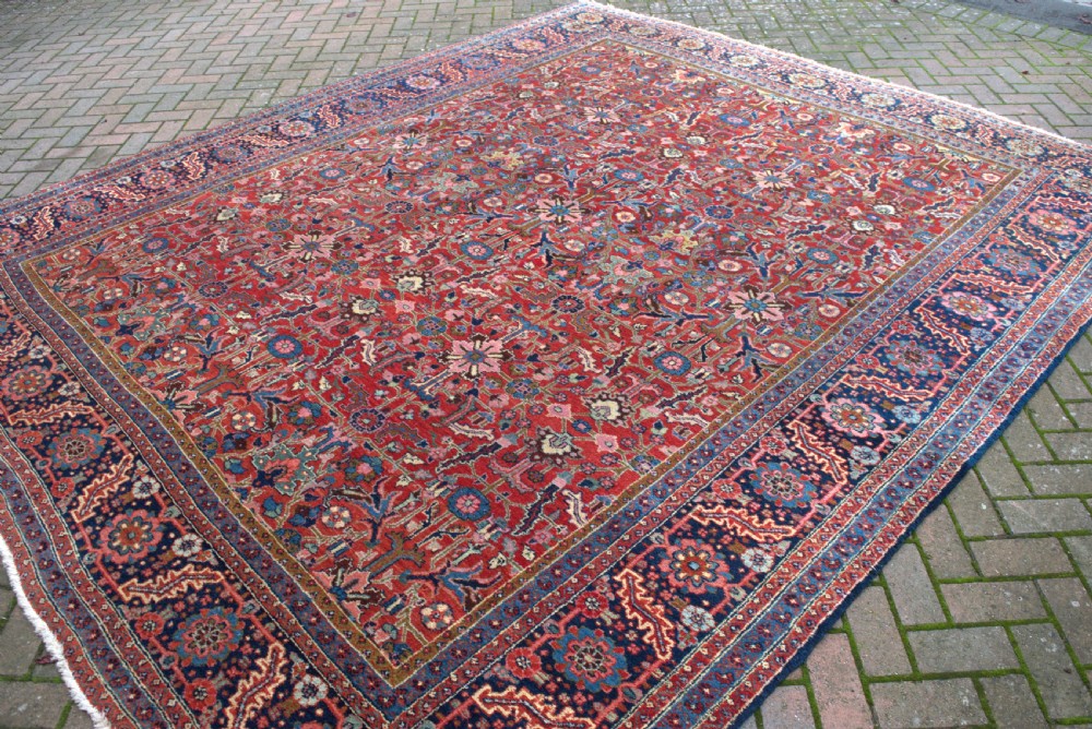 A large hand-knotted wool Heriz carpet featuring an intricate red central field decorated with geometric floral motifs and a dark navy border. View III