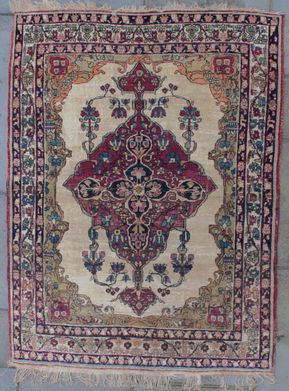 An antique Persian Kirman wool rug featuring a central crimson floral medallion on an ivory field with patterned spandrels and decorative borders.
