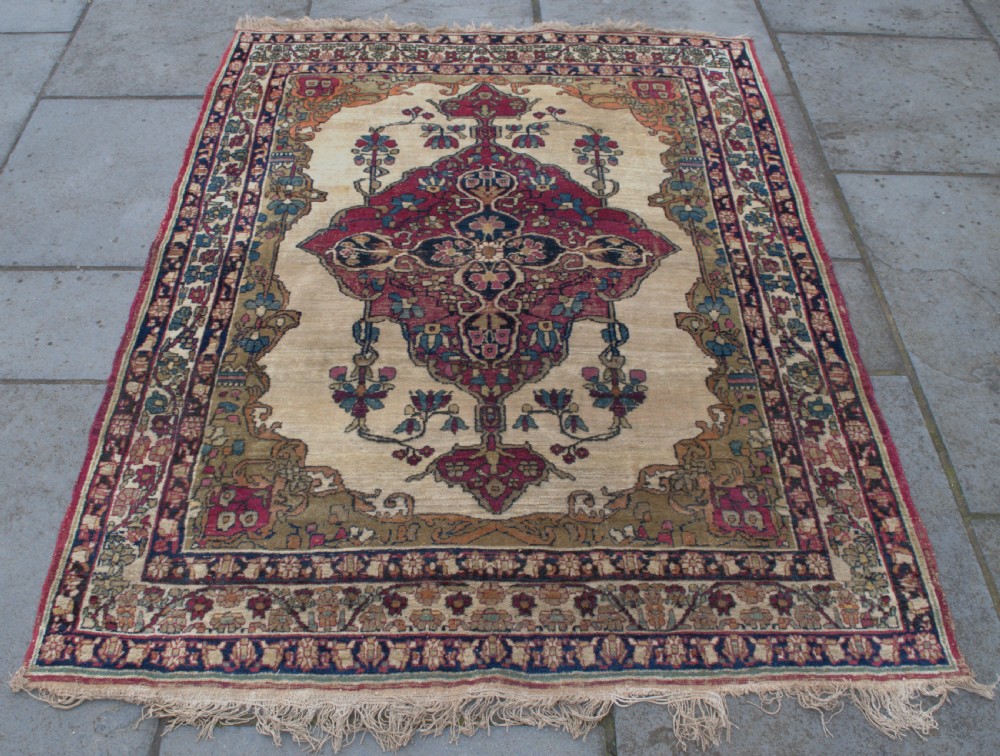 An antique Persian Kirman wool rug featuring a central crimson floral medallion on an ivory field with patterned spandrels and decorative borders. View II