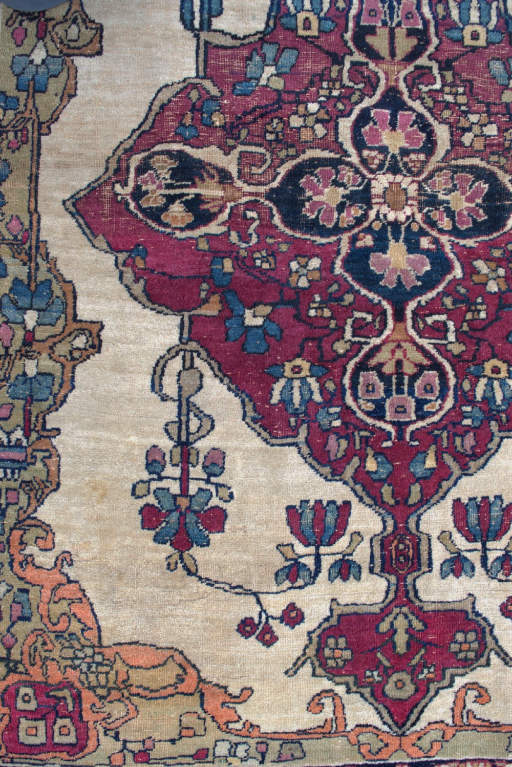 An antique Persian Kirman wool rug featuring a central crimson floral medallion on an ivory field with patterned spandrels and decorative borders. View III