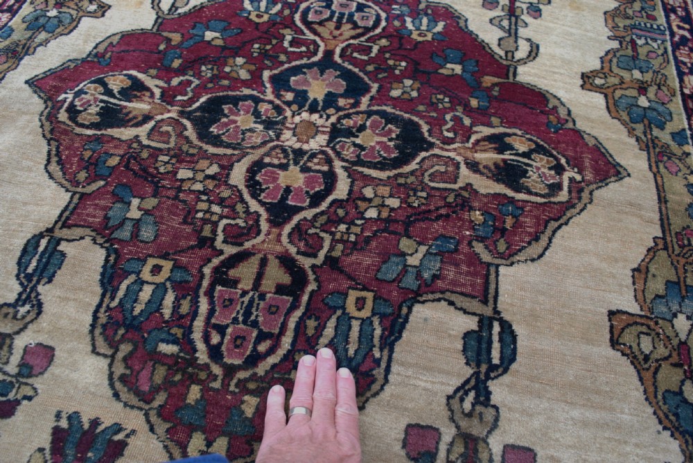 An antique Persian Kirman wool rug featuring a central crimson floral medallion on an ivory field with patterned spandrels and decorative borders. View IV
