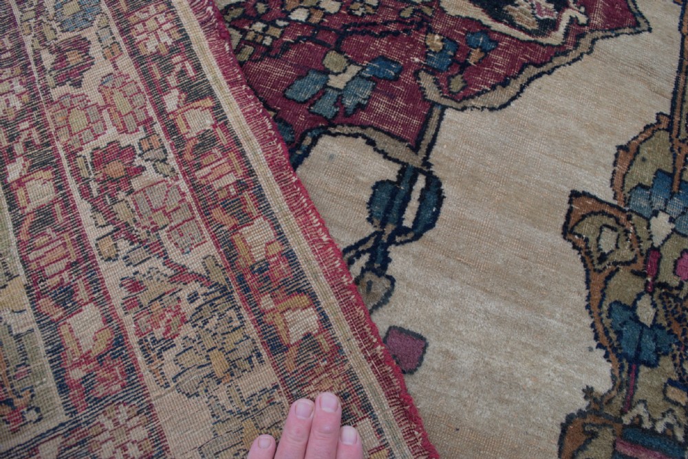 An antique Persian Kirman wool rug featuring a central crimson floral medallion on an ivory field with patterned spandrels and decorative borders. View V