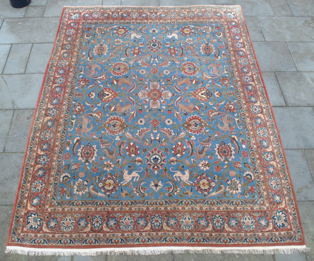 A large hand-knotted wool Veramin carpet featuring a central sky-blue field detailed with animals, birds, and floral vine scrolls inside a red multi-bordered frame.