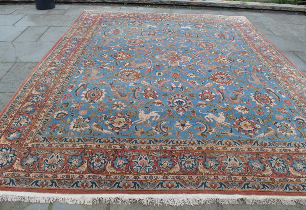 A large hand-knotted wool Veramin carpet featuring a central sky-blue field detailed with animals, birds, and floral vine scrolls inside a red multi-bordered frame. View IV