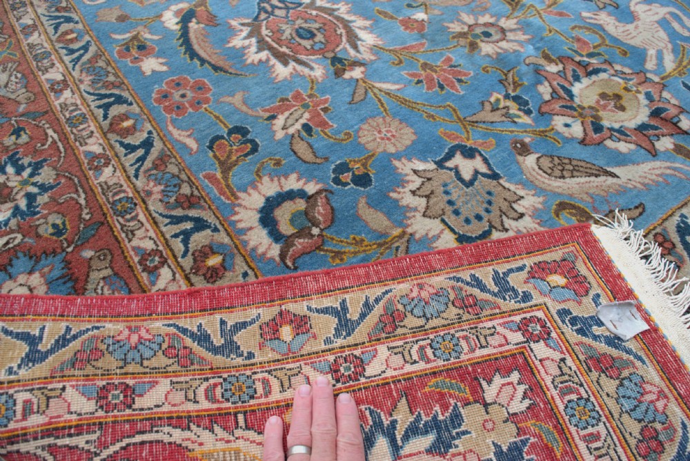 A large hand-knotted wool Veramin carpet featuring a central sky-blue field detailed with animals, birds, and floral vine scrolls inside a red multi-bordered frame. View VII