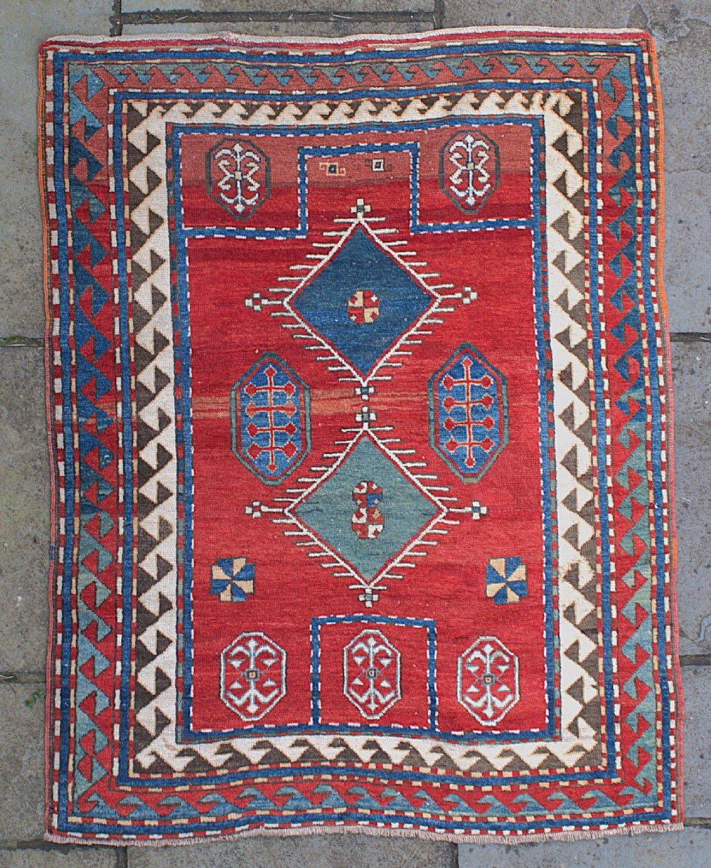 An antique Caucasian Kazak hand-knotted wool prayer rug featuring geometric diamond medallions on a red field framed by multiple patterned borders.
