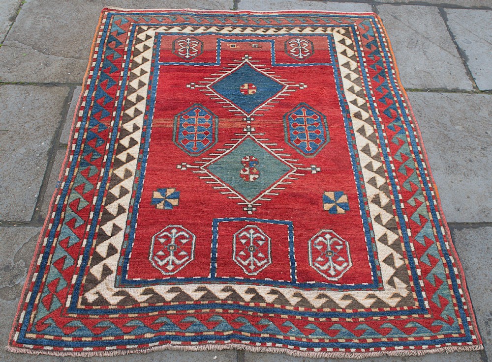 An antique Caucasian Kazak hand-knotted wool prayer rug featuring geometric diamond medallions on a red field framed by multiple patterned borders. View II