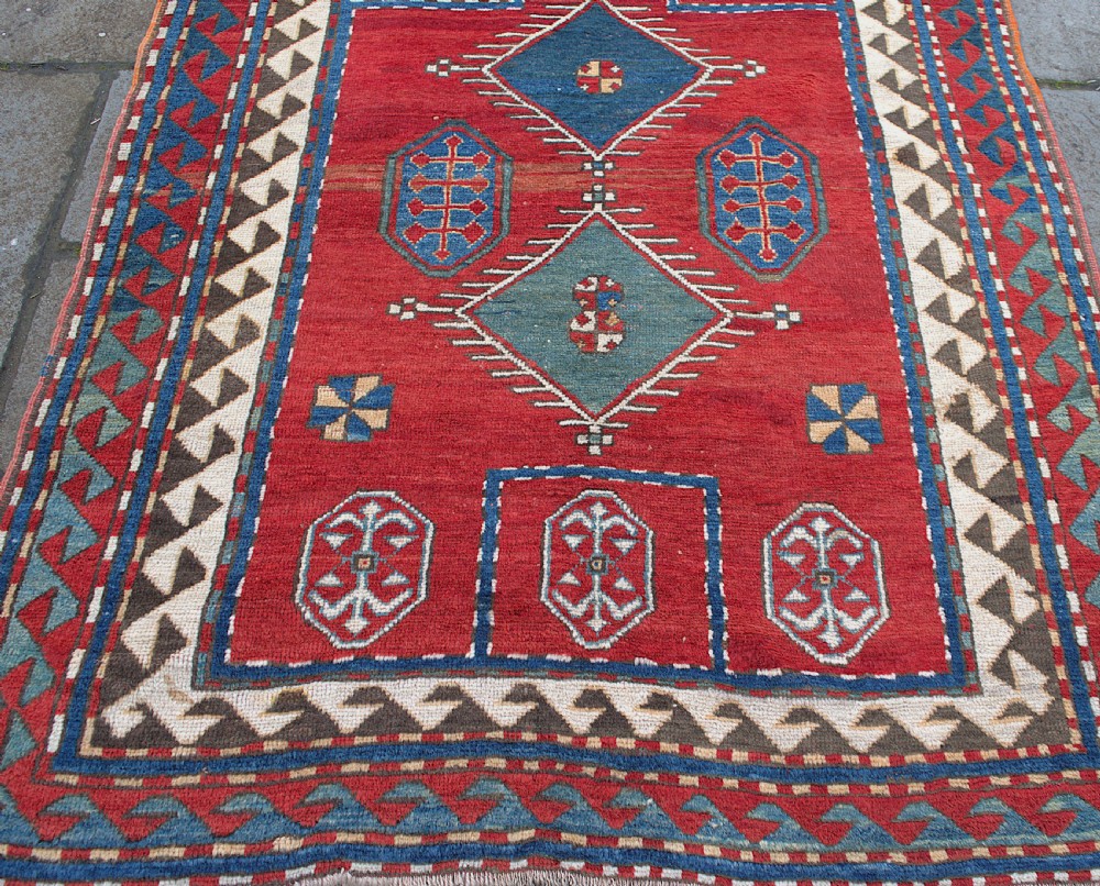 An antique Caucasian Kazak hand-knotted wool prayer rug featuring geometric diamond medallions on a red field framed by multiple patterned borders. View III