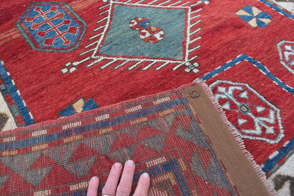 An antique Caucasian Kazak hand-knotted wool prayer rug featuring geometric diamond medallions on a red field framed by multiple patterned borders. View V