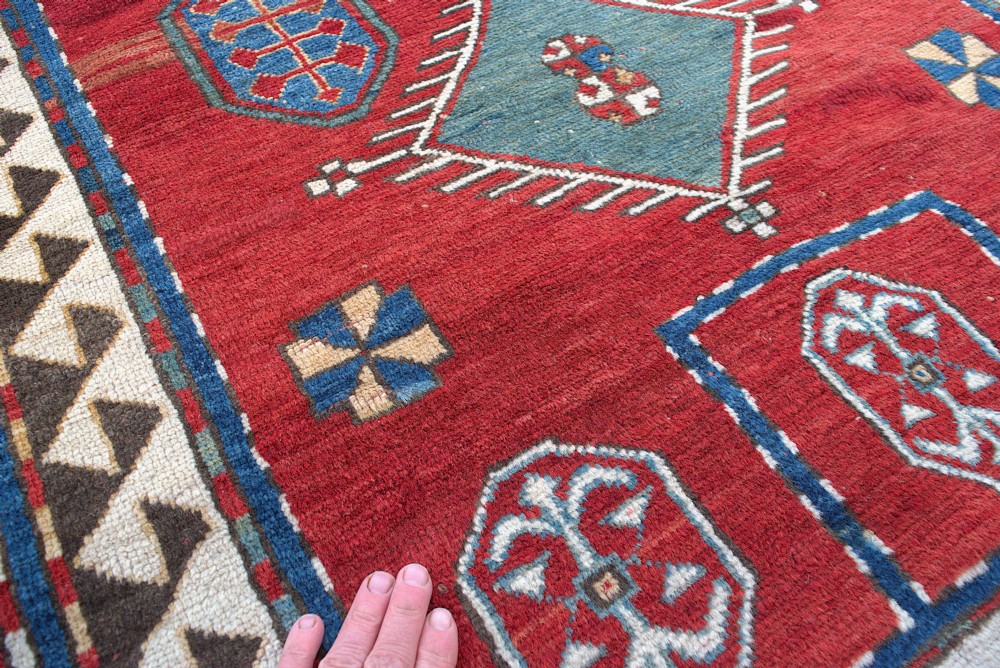 An antique Caucasian Kazak hand-knotted wool prayer rug featuring geometric diamond medallions on a red field framed by multiple patterned borders. View VI