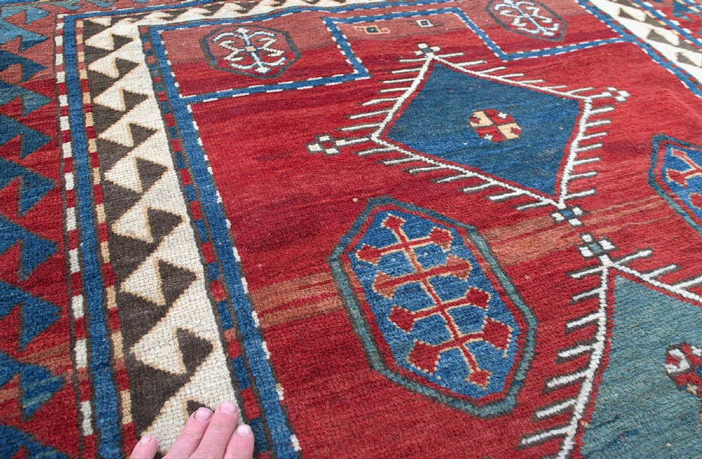 An antique Caucasian Kazak hand-knotted wool prayer rug featuring geometric diamond medallions on a red field framed by multiple patterned borders. View VII