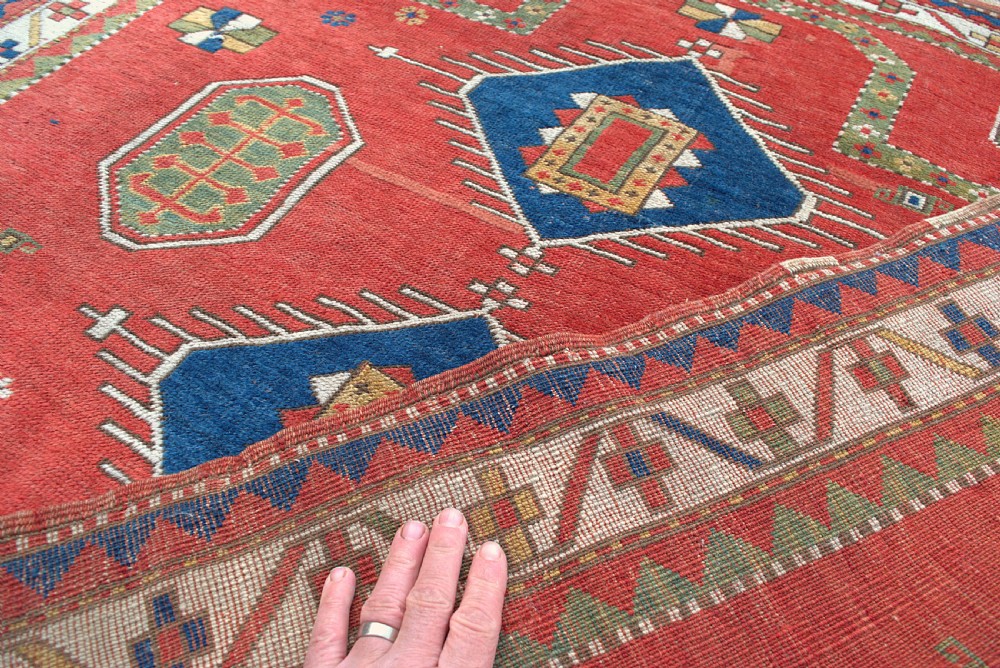 An antique square Kazak wool prayer rug featuring a red ground, central blue diamond medallions, geometric octagonal motifs, and a patterned cream border. View V