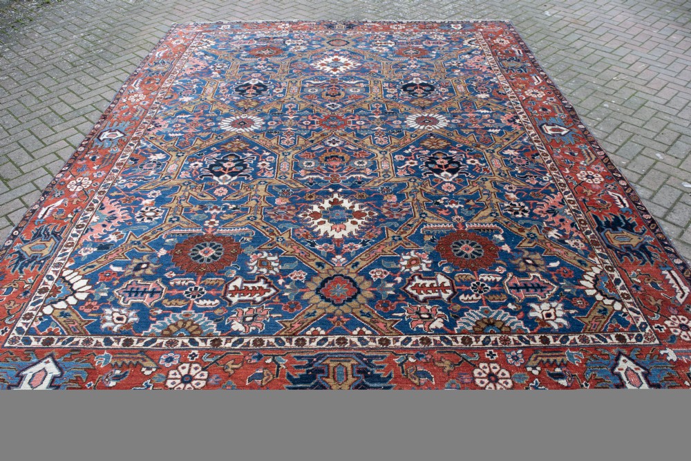 A large hand-knotted antique Heriz wool carpet featuring geometric floral motifs in deep blue, terracotta red, and ivory tones.