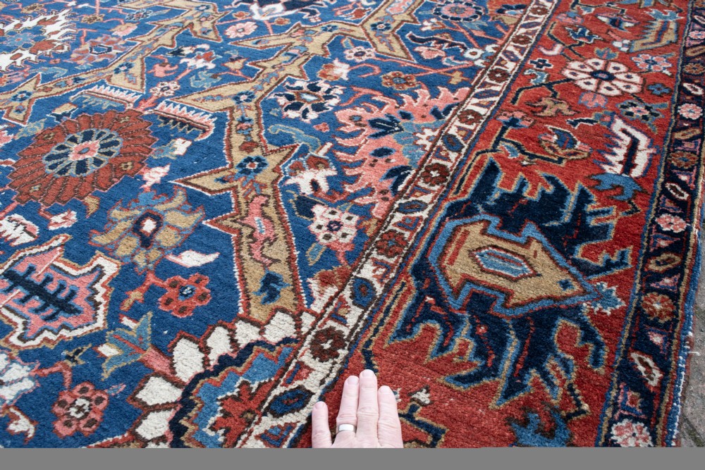 A large hand-knotted antique Heriz wool carpet featuring geometric floral motifs in deep blue, terracotta red, and ivory tones. View VI
