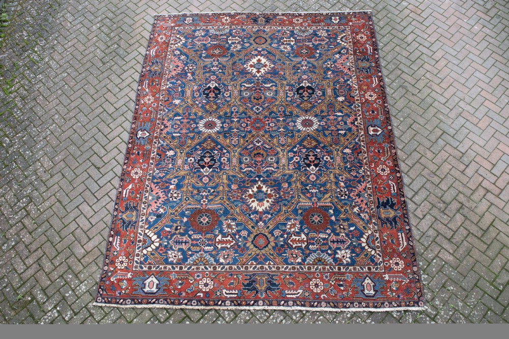 A large hand-knotted antique Heriz wool carpet featuring geometric floral motifs in deep blue, terracotta red, and ivory tones. View VII