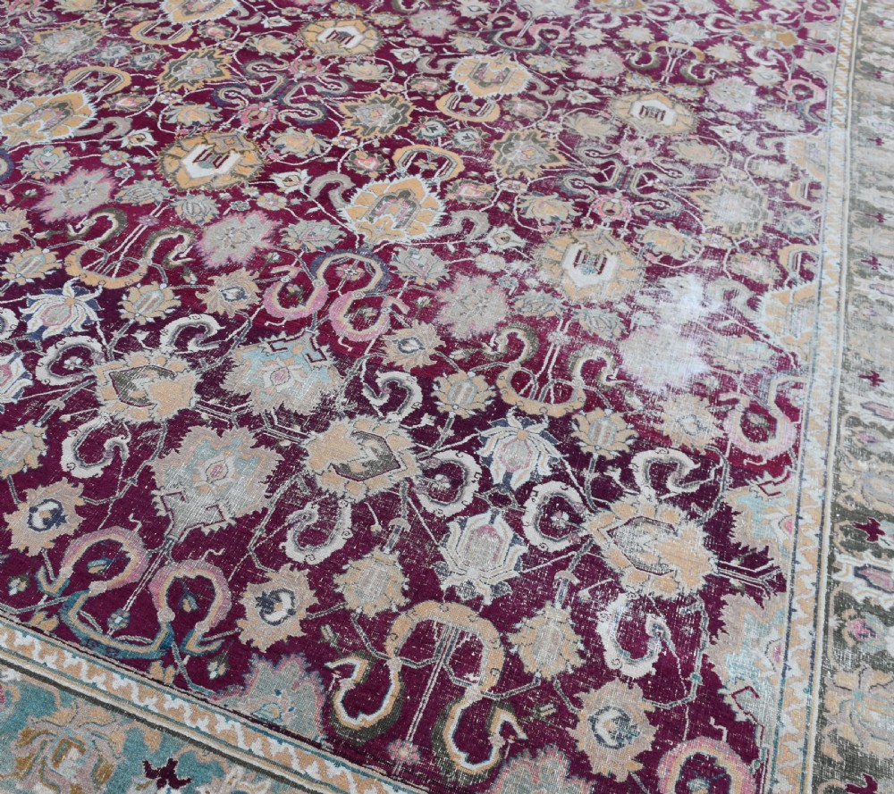 A large rectangular hand-woven wool carpet featuring an intricate floral lattice pattern in plum tones framed by a contrasting sage green decorative border. View III