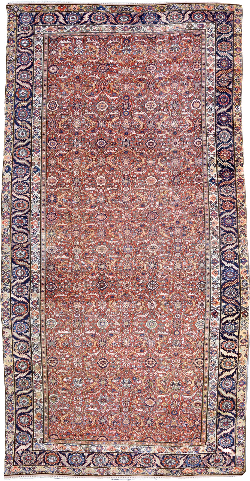 An antique North West Persian wool carpet featuring a repeating geometric floral lattice field on terracotta red, enclosed by a wide navy blue patterned border.
