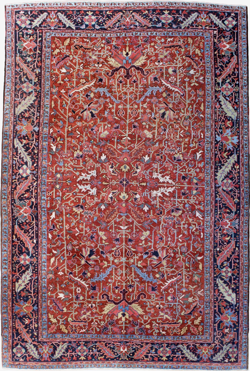 A rectangular hand-knotted Persian Heriz carpet featuring an intricate all-over geometric floral design in terracotta red, light blue, and navy blue tones.
