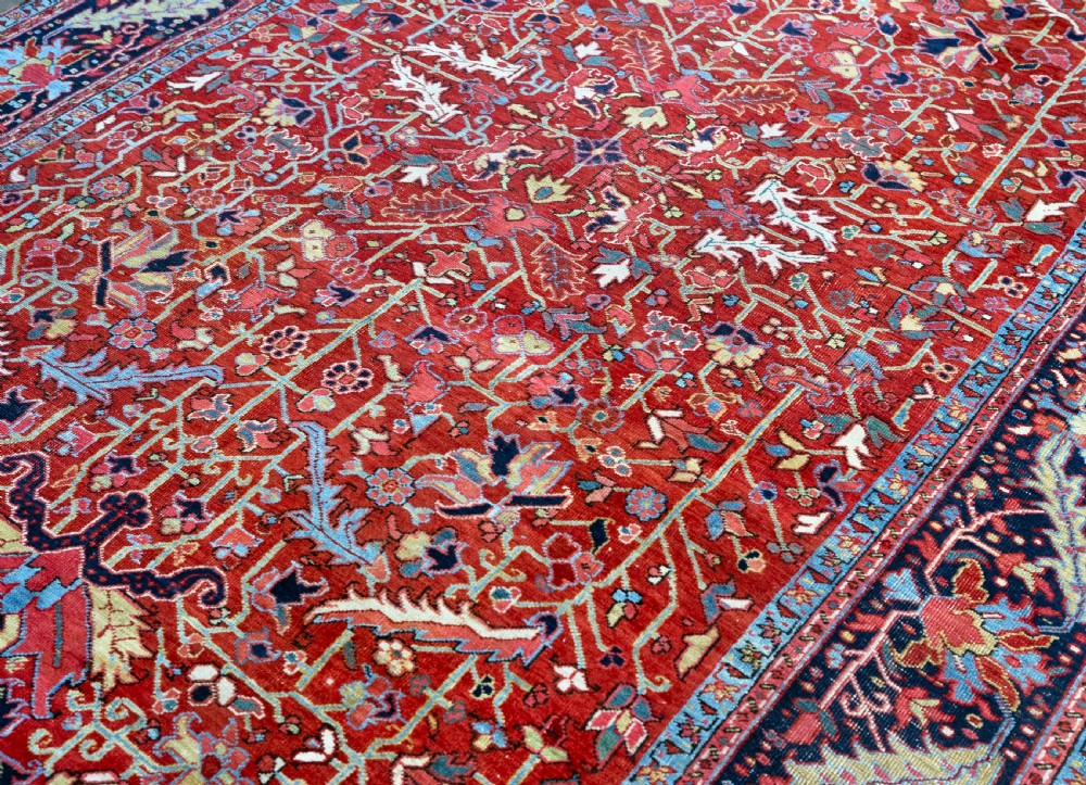 A rectangular hand-knotted Persian Heriz carpet featuring an intricate all-over geometric floral design in terracotta red, light blue, and navy blue tones. View VII