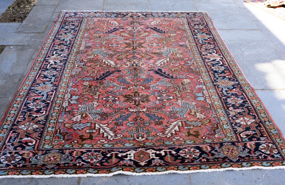 An antique Heriz wool carpet featuring a rust red field with geometric floral patterns framed by a dark navy patterned border. View II