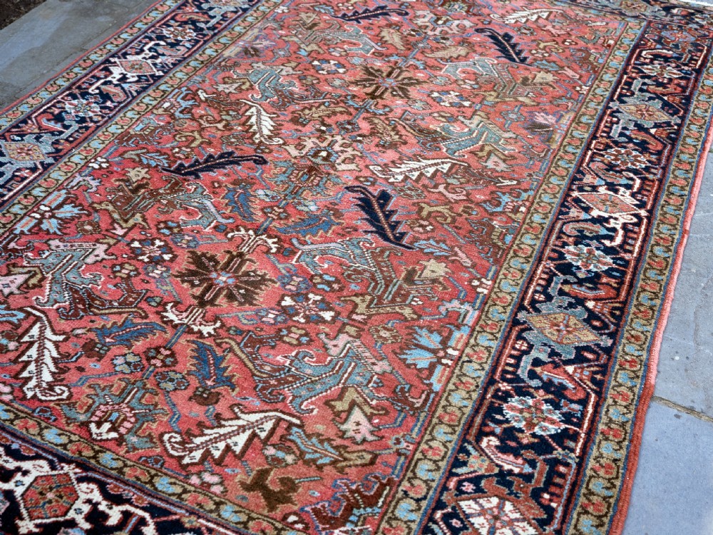 An antique Heriz wool carpet featuring a rust red field with geometric floral patterns framed by a dark navy patterned border. View III
