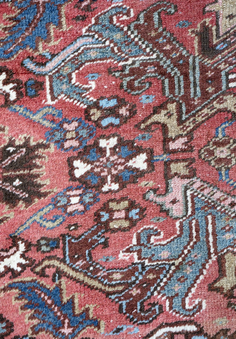 An antique Heriz wool carpet featuring a rust red field with geometric floral patterns framed by a dark navy patterned border. View VI